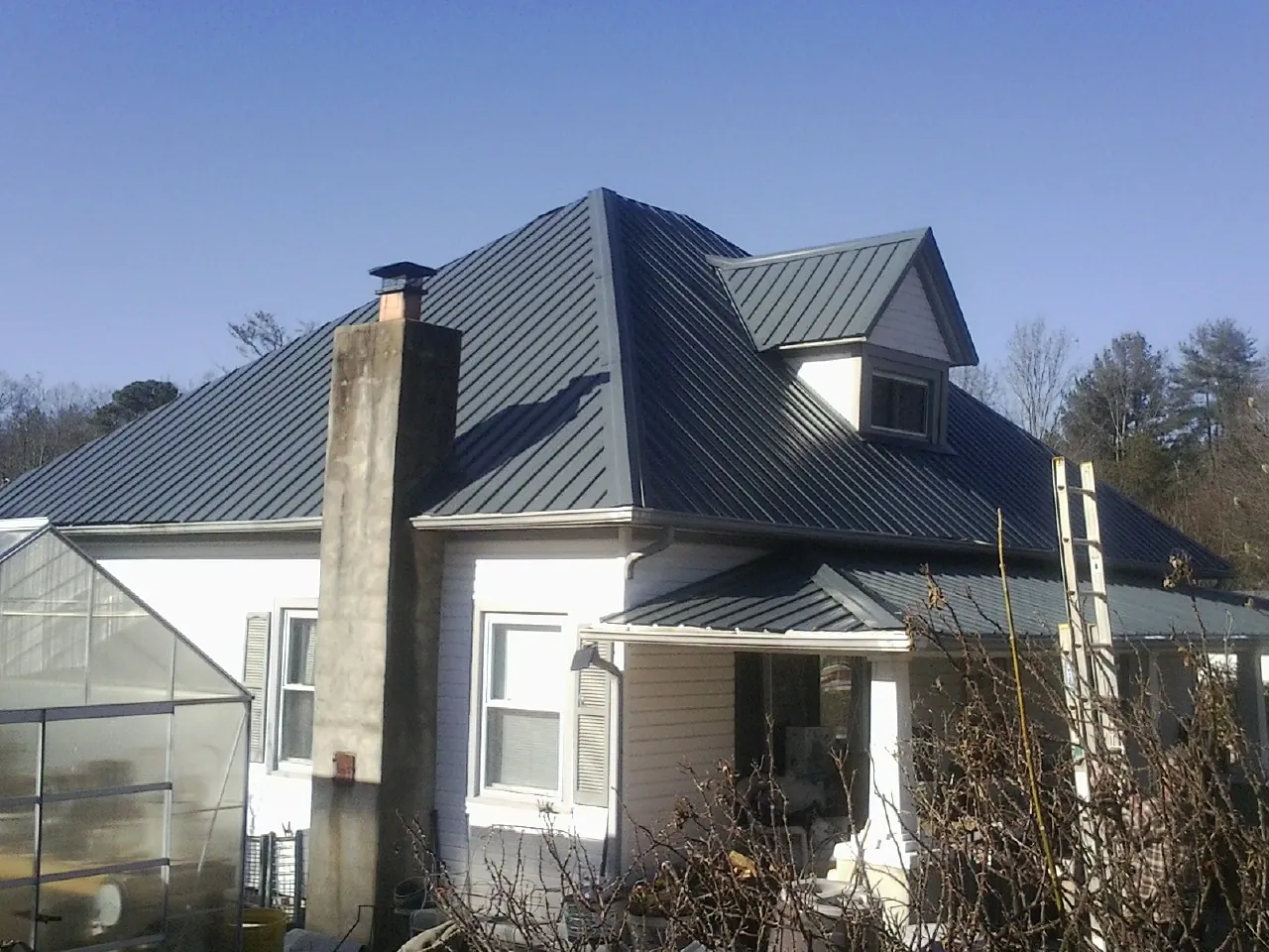 Dark blue standing seam metal roof on a white farmhouse with dormer in Waretown