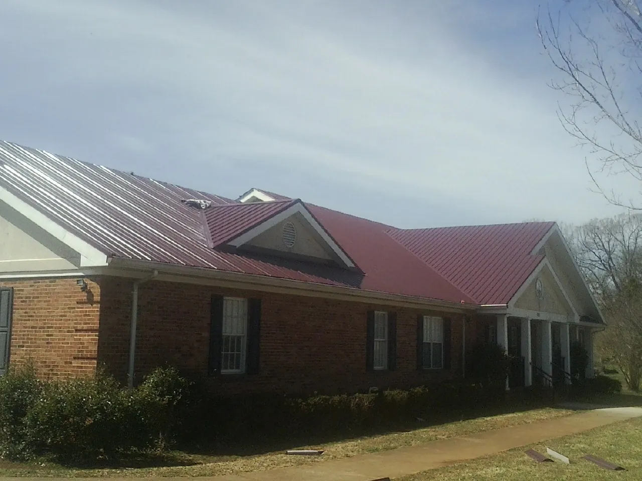 Red metal roof with gabled entries on a long brick building, from a Hail Damage Roof Repair job in Waretown