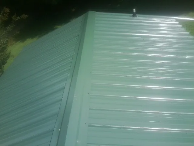 New green metal panels meeting at the ridge of a roof — Flat Roof Repair work by our crew in Waretown