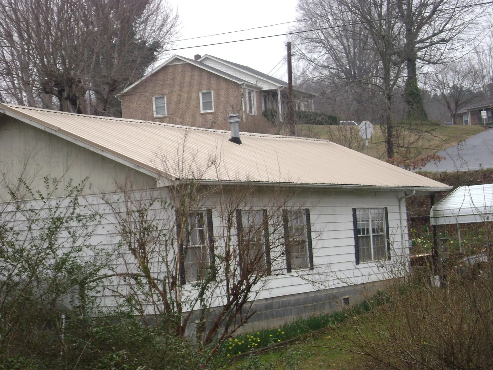 Tan metal roof on a white sided house set into a hillside — Commercial Roofing by Roofing Brothers in Waretown